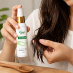 A person holds a bottle of Gyan Plus Hair Serum while touching their long dark brown hair, with a wooden spoon on a table in the foreground.